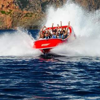 Corse Émotion’s red jet boat in a wall of spray, passengers with arms raised