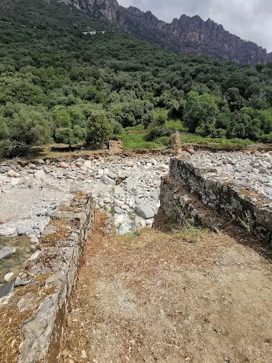 Ruined stone walls beside the riverbed, jagged mountains behind