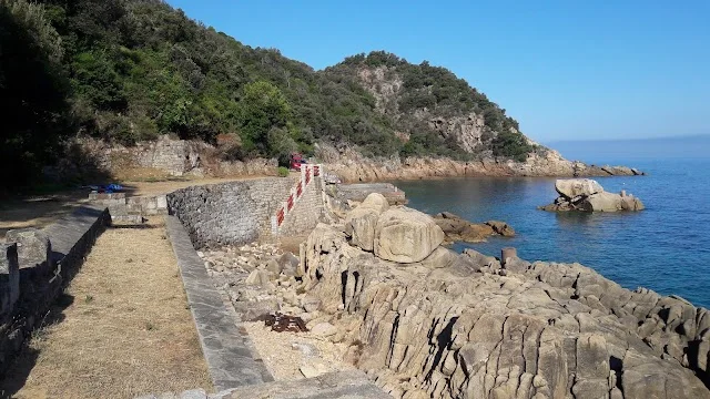 The small harbour of Castagna: stone quay, red and white railing and rocks at the water's edge