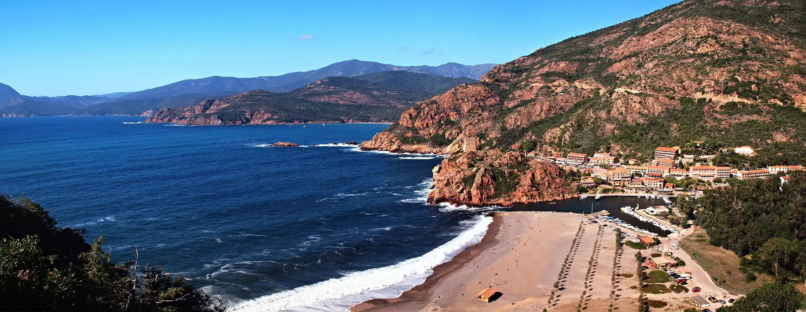 Panorama of the marina of Porto: the beach and its waves, the large tree-lined car park, the harbour and the village